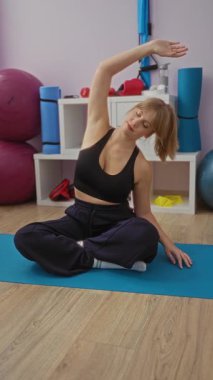 Kadın jimnastik salonunda yoga minderinin üzerinde hareketli fitness ortamının ortasında egzersiz rutini sergiliyor.