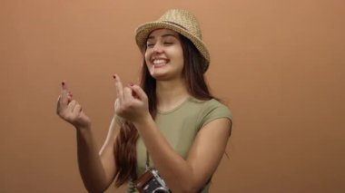 Hasır bir şapkayla gülümseyen İspanyol kadın izole edilmiş kahverengi bir arka plana karşı neşeli bir jest yapıyor, canlı ve anlamlı bir ruh hali yaratıyor..