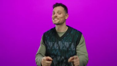 İspanyol bir adam canlı pembe arka planda kameraya neşeli bir şekilde bakıyor, kendine güveni ve çekiciliği yayıyor..