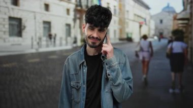 Kot ceketli, sakallı genç adam şehir sokağında telefonda konuşuyor, geçmişi bulanık..