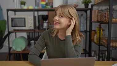 Mutfak aletleriyle çevrili modern kapalı bir çalışma alanında ofis masasında el pençe divan duran gülümseyen kadın..