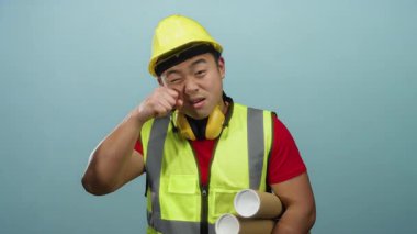 Kasketli ve yelekli genç adam inşaat bağlamında mizah taşıyan beyaz bir geçmişe karşı alaycı bir ağlama hareketi yapıyor..