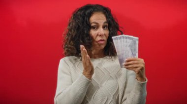 Orta yaşlı bir kadın Filipinli pesoları elinde tutuyor. Yüzünde hoşnutsuzluk var. Kırmızı duvarın arkasında duruyor..