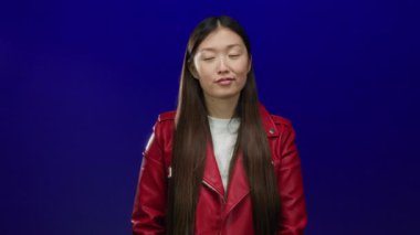 Kırmızı ceketli kadın izole edilmiş mavi arka planda duruyor. Uzun saçlı ve günlük kıyafetleri olan çekici Asyalı bir kadın var..