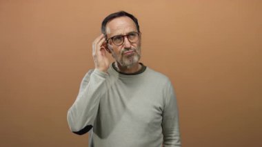 Gayri resmi giyinmiş ve gözlüklü kahverengi arka planda meraklı ve nişanlı bir adam..