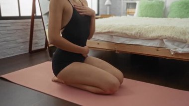 Huzurlu yatak odasında yoga minderi üzerine meditasyon yapan bir kadın. Yumuşak ışıklandırma, rahat bir dekor, somut bir rahatlama ve farkındalık..