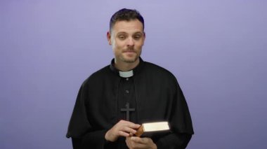 Mor arka planda İncil 'i tutan gülümseyen rahip, dini bağlılık ve inancı vurgulayan modern bir ortamda neşe ve maneviyatı yakalıyor..