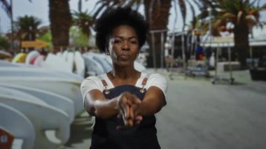 Kadın şehir caddesinde palmiye ağaçları ve sörf tahtalarıyla çevrili bir önlük giyerek parmak tabancası hareketi yapıyor..