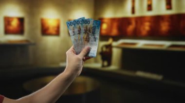 Elinde İsviçre banknotları tutan bir adam müze odasında para ve sanat eserlerini ön plana çıkarıyor..