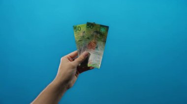 İsviçre ekonomisine odaklı bireyler için finansal kavramları ve döviz döviz potansiyelini tasvir eden, mavi bir zemin üzerinde 50 frank İsviçre banknotları el ele tutuşma.