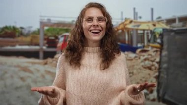 Arka planda makineler olan bir inşaat alanında gülümseyen kadın, dışarıda çalışma ortamında neşe ve rahatlığı somutlaştırıyor..