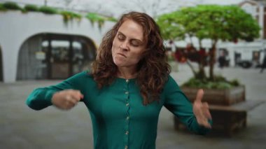 Gündüz vakti arka planda modern mimari ile şehir sokaklarında ifade edilen hareketler yapan kadın.