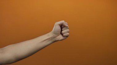 Erkek el, parlak turuncu duvara başparmak işareti veriyor. Bu da temiz, minimalist bir sahnede onaylandığını gösteriyor. Pozitifliği ve kendine güveni canlı bir arka planla vurguluyor..