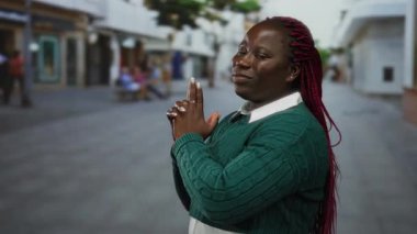 Yeşil kazaklı, kırmızı örgülü bir kadın ıssız bir caddede parmak tabancası jesti yapıyor. Kendine güveni ve oyunculuğu gösteriyor..