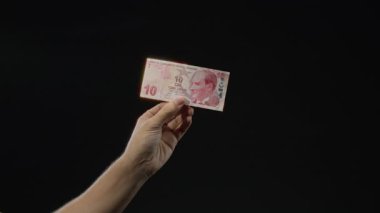 Siyah arkaplan üzerine Türk lirası banknot tutan adam döviz ve finans görüntülerini vurguluyor.