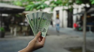 El ele tutuşan Güney Koreli, şehir merkezindeki bir sokak ortamında para ve ekonomik kavramların altını çizerek bulanık arka planda görünen bir adamla birlikte banknotlar kazandı..