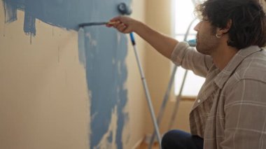 Yeni apartman dairesinde duvar boyayan genç adam ev dekorasyonu ve yaratıcılığını gösteriyor.