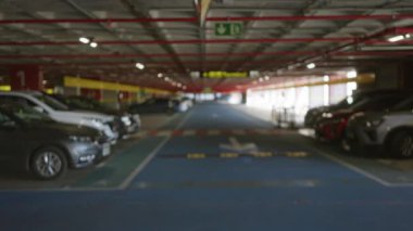 Yapay ışık altında park halindeki sıra sıra park halindeki araçlarla kapalı otopark çok geniş, boş ve sessiz bir alan hissi veriyor..