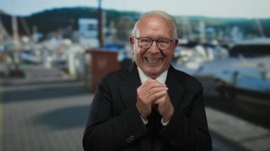 Takım elbiseli kıdemli adam deniz kenarındaki gezinti alanında gülümsüyor, açık hava iş ortamında mutluluk ve başarı sergiliyor.