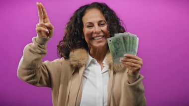 Orta yaşlı bir kadın elinde tek başına para tutuyor ve mor bir geçmişe selam veriyor. Neşe ve finansal başarı yayıyor..