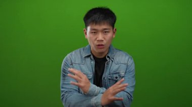 Kot ceketli genç adam, yeşil arka plana karşı olumsuz duygular besliyordu. Elleri çapraz olsun ya da olmasın, bir anlaşmazlık vardı..