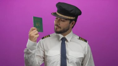 Genç İspanyol pilot yeşil bir pasaport tutuyor canlı pembe bir arka plana karşı, kendine güvenen bir ifadeyle üniforma giymiş..