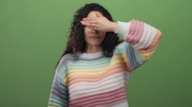 Renkli süveter içinde gülümseyen, yeşil arka planda elleri olan bir kadın, neşe ve samimiyet ifade eder.