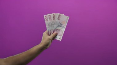 Elinde Türk lira banknotları tutan bir adam, canlı mor bir arka plan gösterme para birimi ile izole edilmiş finansal temalar üzerinde el konseptini gösteriyor.