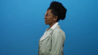 Gözlüklü kadın, izole edilmiş mavi arka plan, iletişim duygusu, odaklanma, ifade ve görsel dil ve mesleki kıyafet yoluyla çeşitlilik üzerine şaşkınlık gösteriyor..