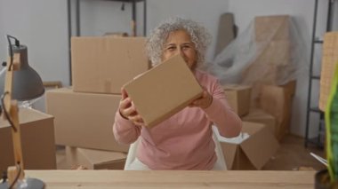 Yeni bir evde, mutlu bir şekilde kutuları açıyor. Oturma odasında kartonla çevrili. Bir daireye taşınmanın sıcaklığını ve heyecanını sergiliyor..