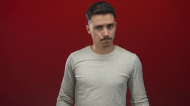 Genç İspanyol bir adam, gürültülü kırmızı bir arka plana karşı kulaklarını kapatır. Sinir bozucu ve yalnızlık ifade eder..