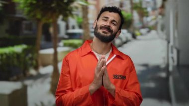 Turuncu hapishane tulumu giyen, sakallı İspanyol bir adam sokakta dikiliyor, duygularını iletiyor ve yalvarıyor..