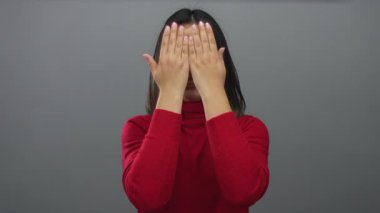 Kırmızı kazaklı, gülümseyen genç Çinli kadın, gri bir arka planda, elleri arkasından yüzünü gösteriyor..