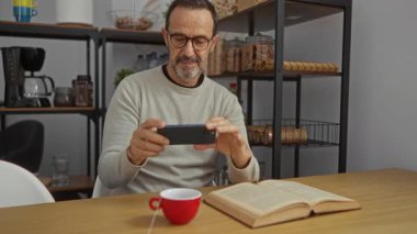 Raflarla, kitaplarla ve kahveyle çevrili rahat çalışma yerinde akıllı telefonlu çay fincanının fotoğrafını çeken adam, her günün görüntülerini yakalıyor..