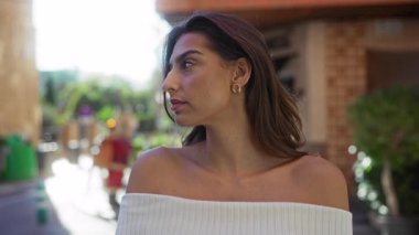 Şehir merkezinde açık havada duran, kumral saçlı, beyaz omuzlu çekici ve kendine güvenen bir kadın. Doğal güneş ışığı altında canlı şehir ortamında..