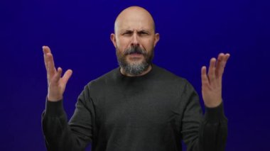 Kel sakallı bir adam, mavi arka plana karşı öfkesini dışa vuruyor, yüz ifadesi ve hareketlerinde duygu ve yoğunluk ifade ediyor..