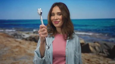 Arka planda sakin deniz olan güneşli sahil sahilinde ingiliz anahtarı tutan genç İspanyol kadın..