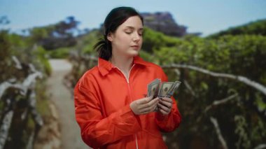 Turuncu eşofmanlı, esmer saçlı, bize dolar tutan bir kadın yemyeşil bir sahil boyunca yürüyor..