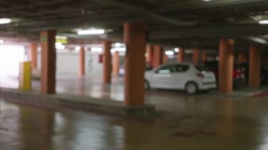 Kapalı bir yeraltı garajında beton sütunlu kapalı arabaları ve bokeh ışıkları olan bulanık park yeri.