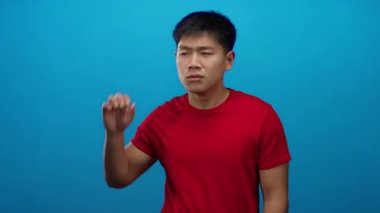 Kırmızı gömlekli genç adam stüdyo ortamında mavi arka plan duvarına karşı dikkatle dinliyor..