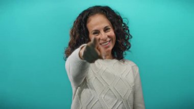 Olgun bir kadın neşeyle gülümsüyor ve kıvırcık saçlarıyla neşeli mavi bir arkaplanda neşeli bir ifadeyle pozitiflik ve güzellik sergiliyor..