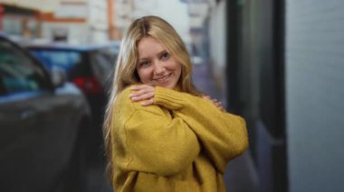 Güneşli bir günde, şehir sokaklarında rahat sarı bir süveter giyen, rahat bir pozla sıcak ve sıradan bir şehir atmosferini yakalayan bir kadın..