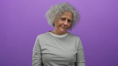 Gri saçlı bir kadın canlı mor bir arka plana karşı duruyor. Tarafsız bir gömlek giyiyor, çeşitli duygular ifade ediyor. Olgun güzellik ve kendine güven sergiliyor..
