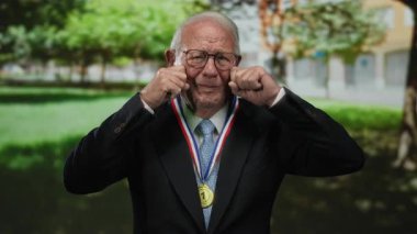 Takım elbiseli kıdemli bir adam parkta ağlıyormuş gibi yapıyor, duygularını ve başarılarını açık havada sergiliyor..