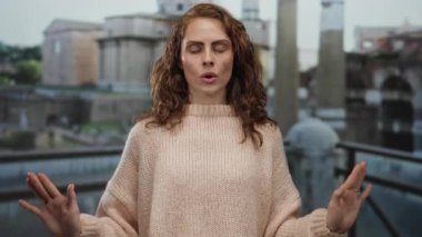 Roma harabelerinde sakince meditasyon yapan, rahat süveter giyen, eski şehir zeminine karşı duruş sergileyen, tarihi mimarinin ortasında sükuneti anımsatan bir kadın..