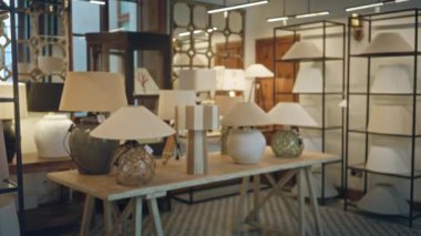 Dükkanın içi, raflarla çevrili ahşap bir masanın üzerinde çeşitli masa lambaları sergiliyor, modern bir bokeh etkisi ile sıcak, samimi ve odaklanmış bir arka plan ortamı yaratıyor..