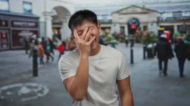 Kalabalık bir caddede gülen genç bir adam ve parlak bir günde arka planda yürüyen insanlar.