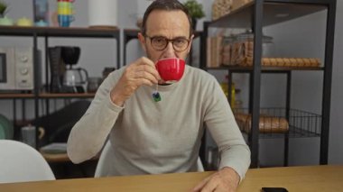 Modern ofis ortamında kahve içen adam, raflar ve mutfak aletleriyle çevrili, sakin, olgun bir tarzı canlandırıyor..