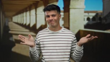 Çizgili süveter giyen genç bir adam tarihi üniversite avlusunda kemerli koridorlar, güneş ışığı altında mizah ile bir araya gelen cazibe.