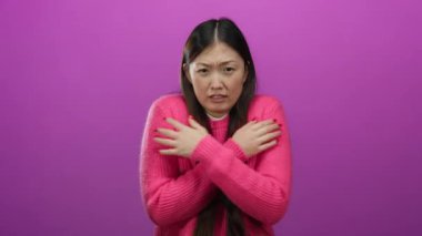 Pembe bir arka planda pembe kazak giyen kadın soğuk ve titrek görünür, kollarını kavuşturup, ellerini sıkarak duygularını ifade eder, kış modasını ve havasını ön plana çıkarır..